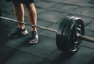 Close-up of a man deadlifting a heavy barbell in an indoor gym setting.